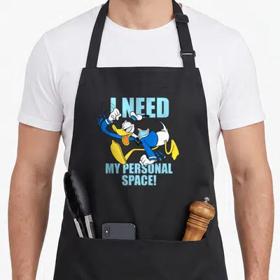 Tablier de cuisine noir avec Donald Duck en course et le texte I NEED MY PERSONAL SPACE en bleu clair.