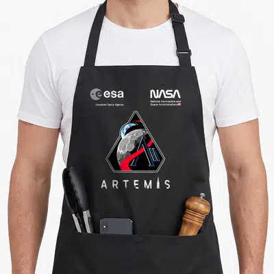 Tablier de cuisine noir avec le logo Artemis II, les insignes NASA et ESA imprimés en blanc et couleurs.