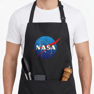 Tablier de cuisine noir avec le logo NASA en cercle bleu, texte blanc, aile rouge et étoiles dispersées.
