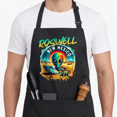 Tablier de cuisine noir avec illustration d'un alien vert, d'un vaisseau spatial et des mots Roswell New Mexico sur fond désertique.