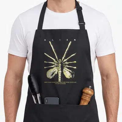 Tablier de cuisine noir avec illustration Facehugger jaune et texte Once Again Something Has Come From Space and It's Not A Friend.
