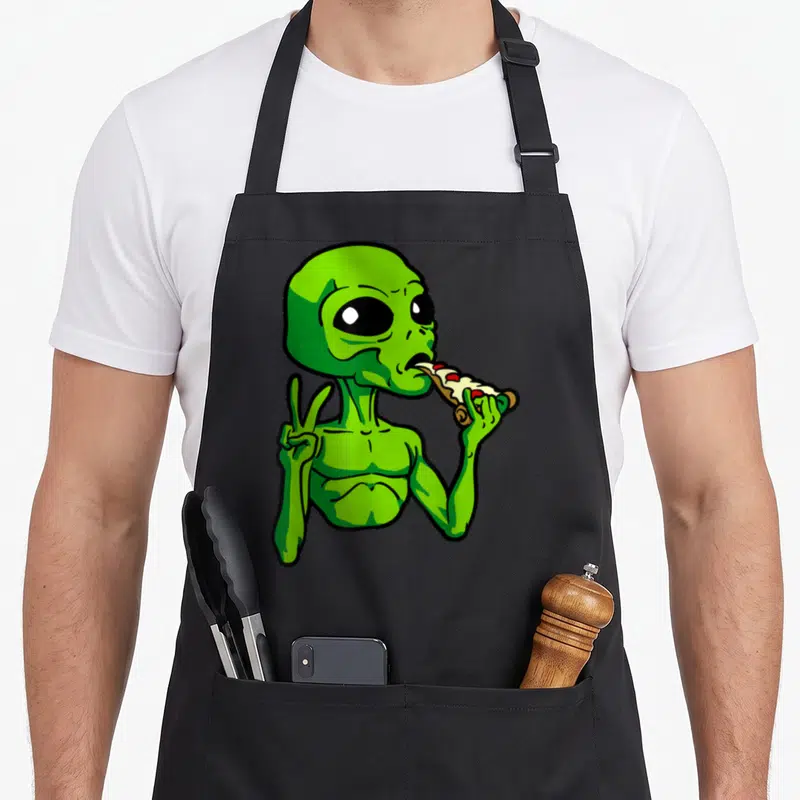 Tablier de cuisine noir avec un alien vert mangeant une pizza et faisant un signe de paix.