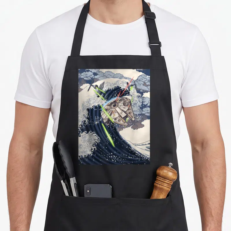 Tablier de cuisine noir avec illustration du vaisseau Millennium Falcon sur une grande vague style gravure japonaise et des lasers verts.