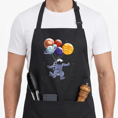 Tablier de cuisine noir avec un astronaute suspendu à des ballons représentant divers planètes du système solaire.