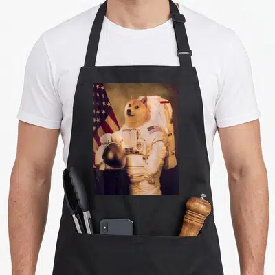 Tablier de cuisine noir avec illustration d'un chien astronauta tenant un casque devant un drapeau américain.