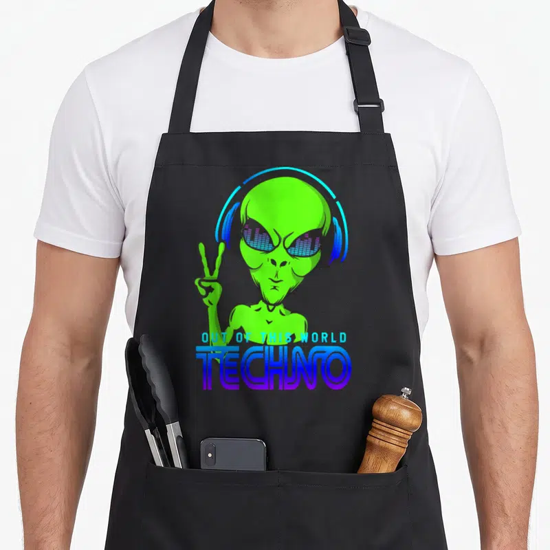 Tablier de cuisine noir avec un alien vert portant des écouteurs bleus et faisant un signe de la paix sous le mot Techno.