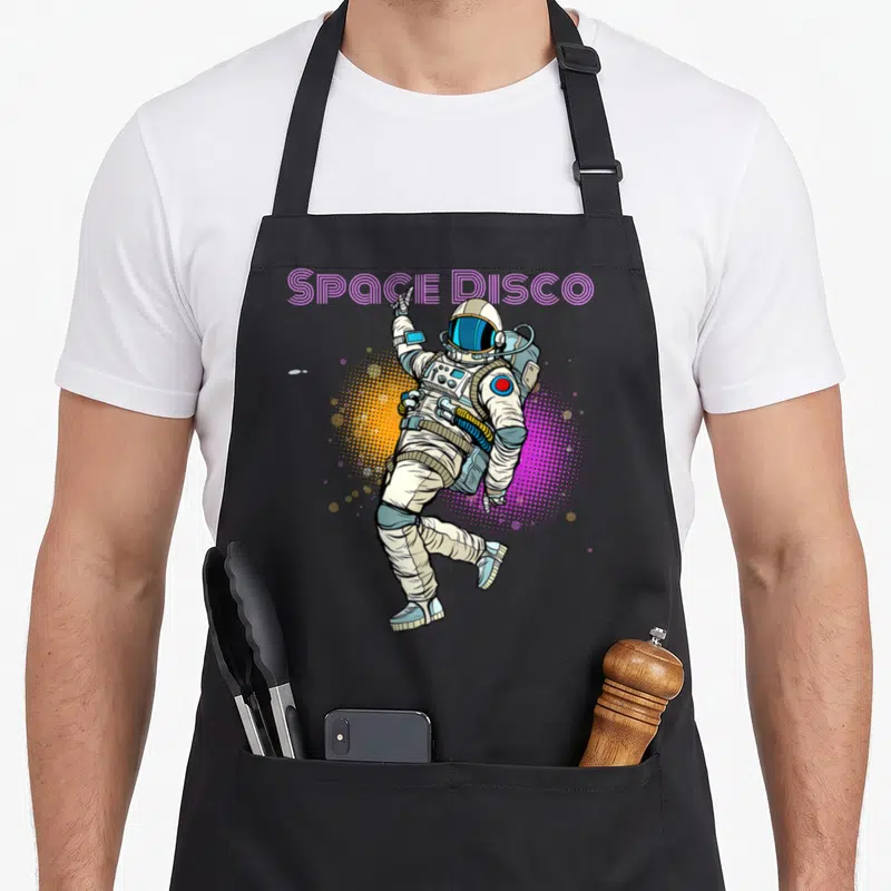 Tablier de cuisine noir avec illustration d'un astronaute dansant sous l'inscription Space Disco en rose néon.