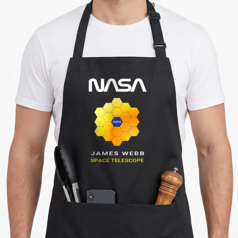 Tablier de cuisine noir avec le logo NASA et l'illustration hexagonale dorée du télescope spatial James Webb.