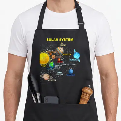 Tablier de cuisine noir avec illustration colorée du système solaire et des noms des planètes en anglais.