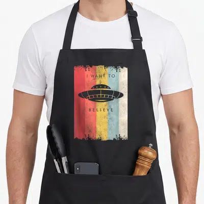 Tablier de cuisine noir avec illustration vintage d'une soucoupe volante sur fond de bandes rouges, jaunes et bleues.