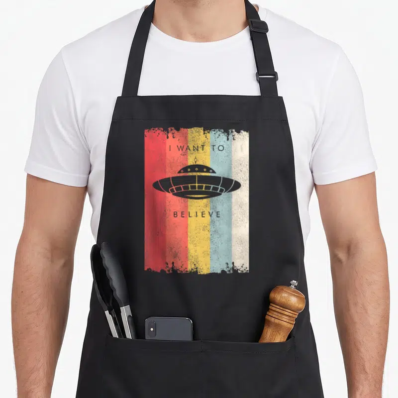 Tablier de cuisine noir avec illustration vintage d'une soucoupe volante sur fond de bandes rouges, jaunes et bleues.