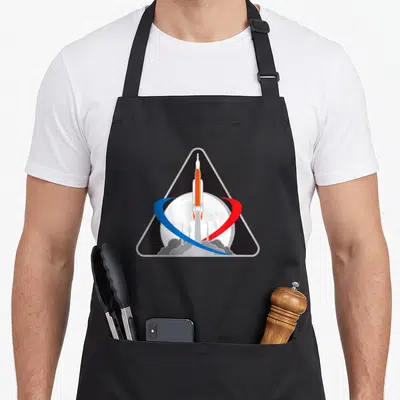 Tablier de cuisine noir avec le logo triangulaire du lanceur Orion SLS Artemis 1 devant la Lune et des orbites rouge et bleue.