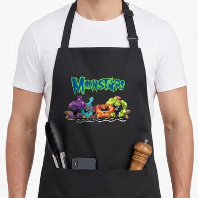 Tablier de cuisine noir avec le logo Monstars et quatre monstres colorés assis sur un banc en bois.