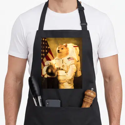 Tablier de cuisine noir avec un Shiba Inu en combinaison spatiale tenant son casque devant le drapeau américain.