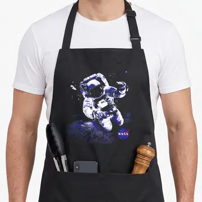 Tablier de cuisine noir avec illustration bleue d'un astronaute en apesanteur et le logo NASA en bas à droite.