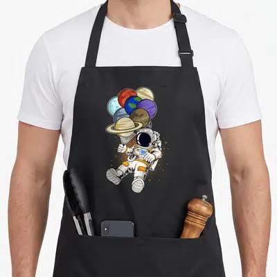Tablier de cuisine noir avec un cosmonaute tenant des ballons représentant les planètes du système solaire.