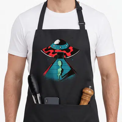 Tablier de cuisine noir avec illustration d'un alien vert montant par une rampe vers un vaisseau spatial rouge et noir.