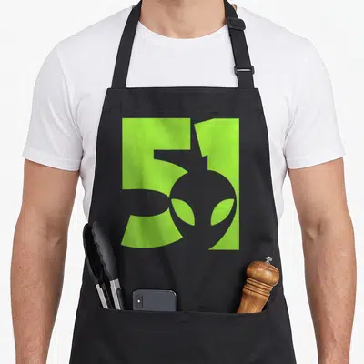 Tablier de cuisine noir avec motif graphique vert lime affichant le chiffre 51 et une silhouette d'alien aux yeux allongés.