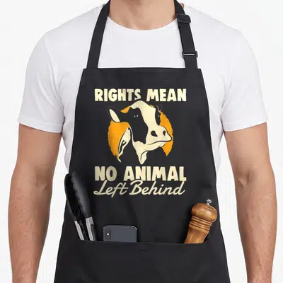 Tablier de cuisine noir avec illustration de tête de vache et texte Rights Mean No Animal Left Behind sur fond orange.