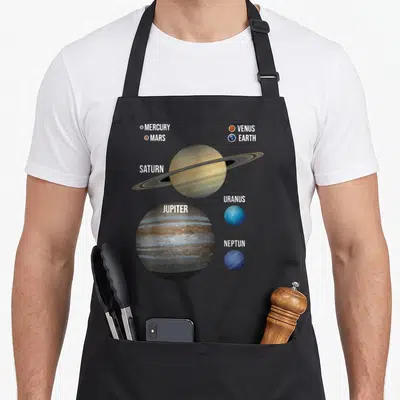 Tablier de cuisine noir avec illustration colorée des planètes du système solaire et leurs noms en lettres capitales blanches.