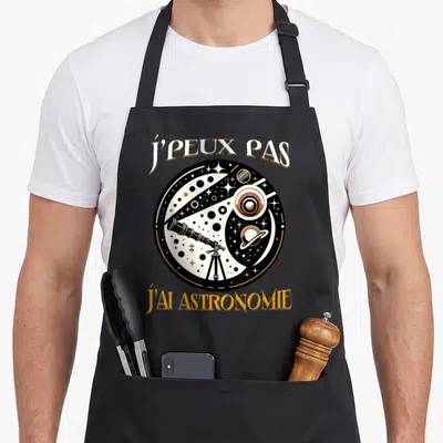 Tablier de cuisine noir avec illustration circulaire montrant un télescope, des étoiles et des planètes sur fond cosmique.