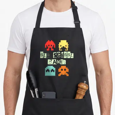 Tablier de cuisine noir avec quatre aliens pixelisés colorés et le texte Old School Gamer en typographie vintage délavée.