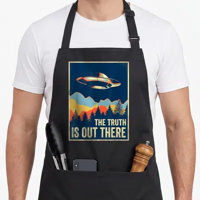 Tablier de cuisine noir avec illustration d'un ovni au-dessus de montagnes et forêts sous le texte The Truth Is Out There.