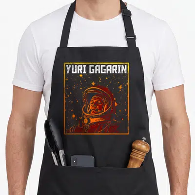 Tablier de cuisine noir avec illustration vintage de Youri Gagarin en casque spatial et texte blanc Yuri Gagarin encadré d'orange.