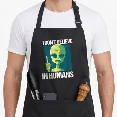 Tablier de cuisine noir avec un extraterrestre vert levant le majeur et le texte I Don't Believe In Humans en blanc.