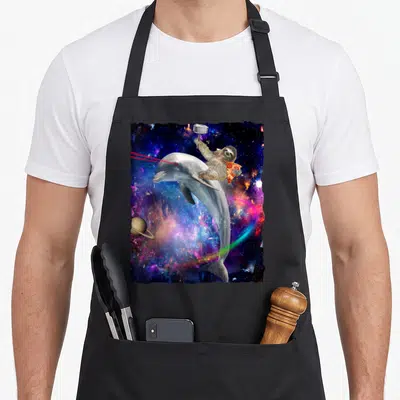 Tablier de cuisine noir avec dauphin spatial, paresseux, pizza et marteau sur fond de nébuleuse colorée.