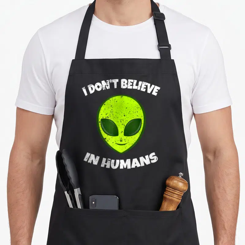 Tablier de cuisine noir avec tête d'alien verte et texte blanc délavé I DON'T BELIEVE IN HUMANS.