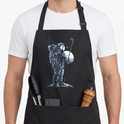 Tablier de cuisine noir avec illustration bleue d'un astronaute prenant un selfie sur la surface lunaire.