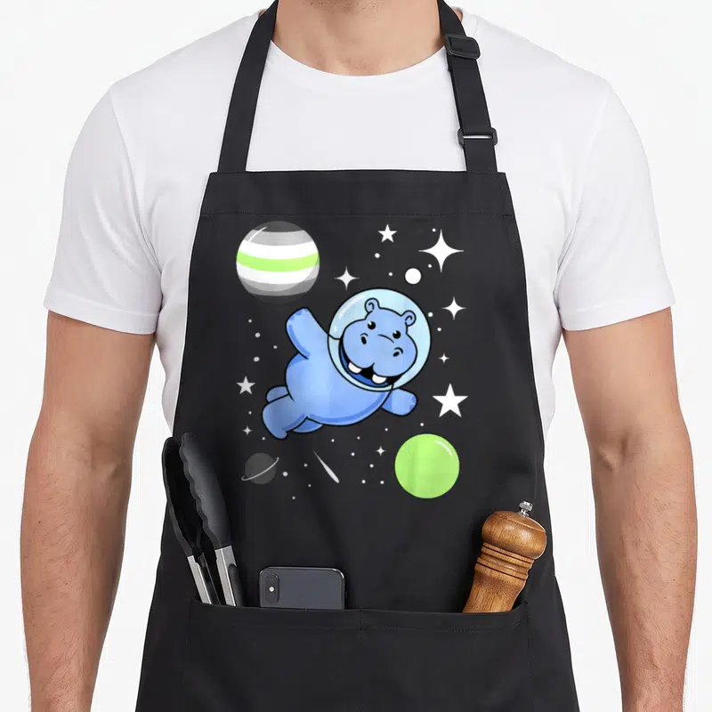 Tablier de cuisine noir avec un hippopotame astronaute bleu souriant au milieu des étoiles et des planètes colorées.