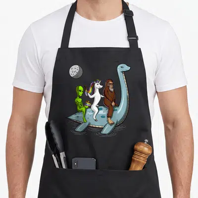 Tablier de cuisine noir avec une licorne, un Bigfoot, un alien vert et le Monstre du Loch Ness sur une montgolfière bleue.