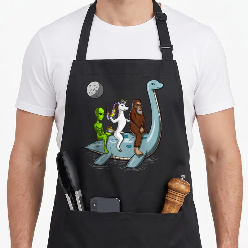 Tablier de cuisine noir avec une licorne, un Bigfoot, un alien vert et le Monstre du Loch Ness sur une montgolfière bleue.
