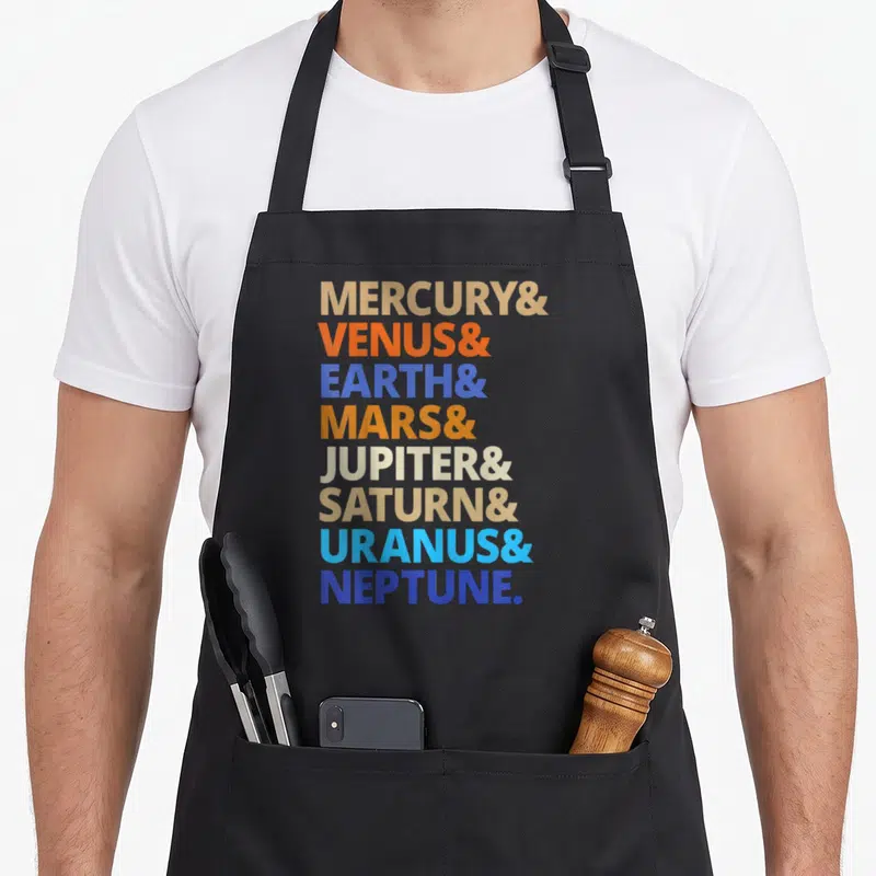 Tablier de cuisine noir avec les noms des planètes du système solaire imprimés en lettres de couleurs vives disposées verticalement.