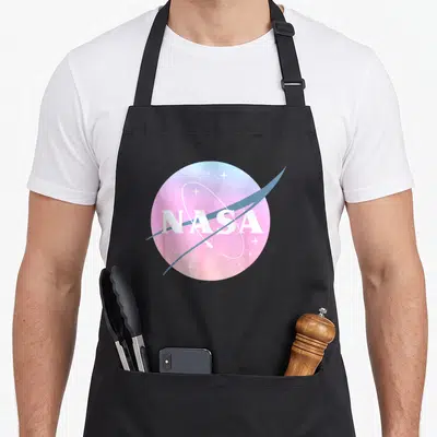 Tablier de cuisine noir avec un logo rond pastel rose et bleu portant l'inscription NASA et des étoiles blanches.