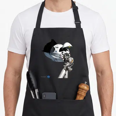 Tablier de cuisine noir avec illustration détaillée de la capsule Dragon SpaceX et logo NASA en bas à gauche.