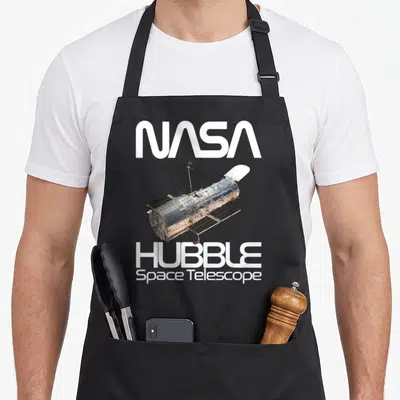 Tablier de cuisine noir avec illustration du télescope spatial Hubble et logos NASA en blanc.