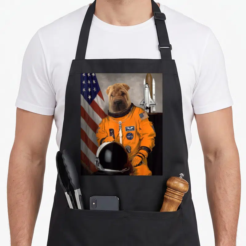 Tablier de cuisine noir avec illustration d'un chien Shar-Pei vêtu d'une combinaison spatiale orange.