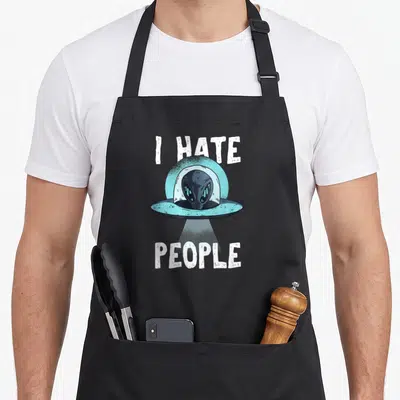 Tablier de cuisine noir avec un extraterrestre dans un engin volant et le texte « I HATE GENS » en blanc.