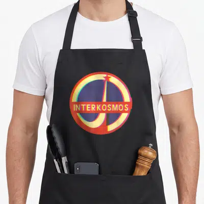 Tablier de cuisine noir avec un logo circulaire Interkosmos aux couleurs vives et une étoile rouge sur fond bleu foncé.