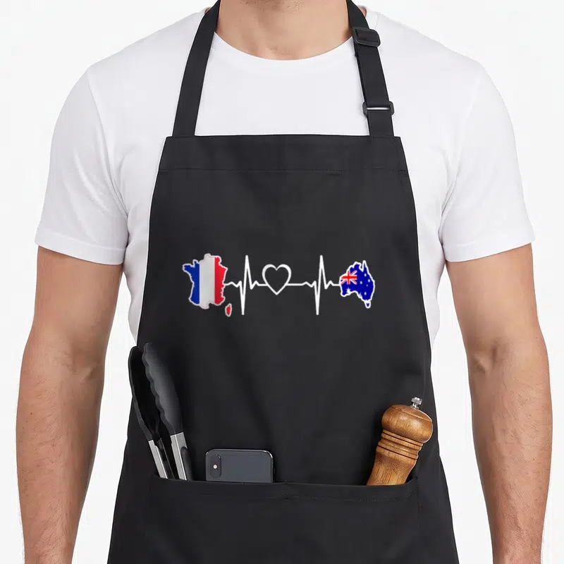 Tablier de cuisine noir avec carte de France et Australie reliées par une ligne de rythme cardiaque blanche.
