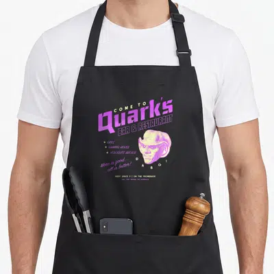 Tablier de cuisine noir avec logo vintage Quarks Bar Restaurant illustration Dabo et texte Deep Space 9 en violet et jaune