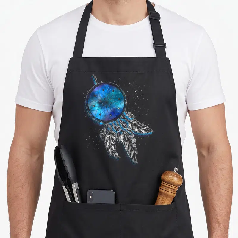 Tablier de cuisine noir avec attrape-rêves indien contenant une galaxie bleue et des plumes blanches stylisées.