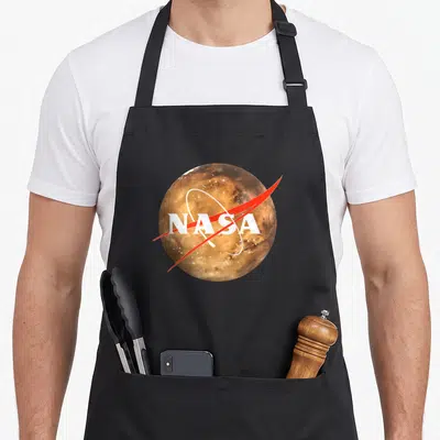 Tablier de cuisine noir avec logo NASA blanc et rouge sur une planète orange texturée et des étoiles scintillantes.