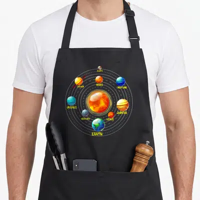 Tablier de cuisine noir avec illustration colorée des planètes du système solaire et leurs noms en lettres jaunes disposés sur des orbites circulaires.