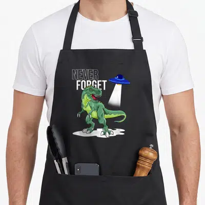 Tablier de cuisine noir avec dinosaure vert et vaisseau spatial bleu émettant un rayon lumineux.