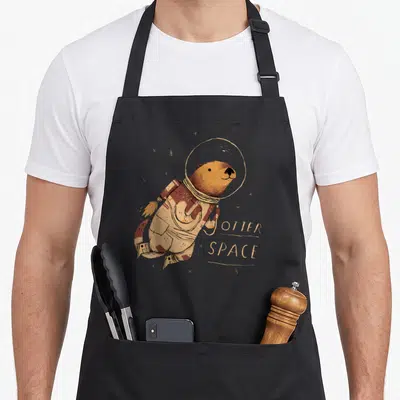 Tablier de cuisine noir avec illustration d'un loutre en combinaison spatiale et texte Otter Space.