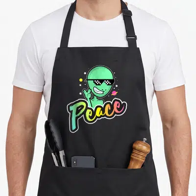 Tablier de cuisine noir avec un alien vert aux lunettes pixel et le mot Peace en lettres colorées.